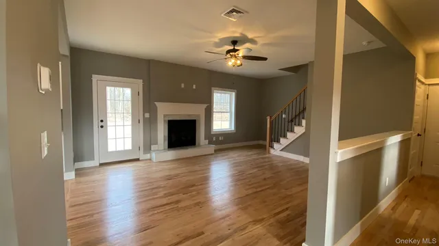 a view of a livingroom with wooden floor a ceiling fan and staircase