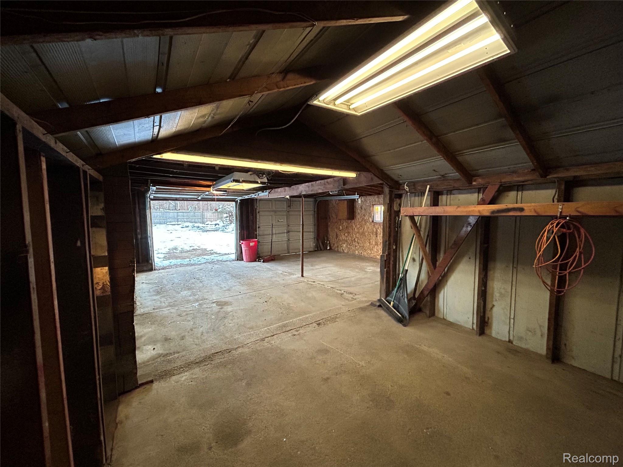 3040 Reeder Road Clarkston, MI 48346 - Photo 10 of 10 Two-car garage space with exposed wood beam ceiling, concrete flooring, and fluorescent lighting fixtures