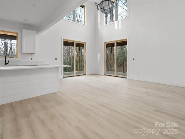 a view of an empty room with chandelier fan and kitchen view
