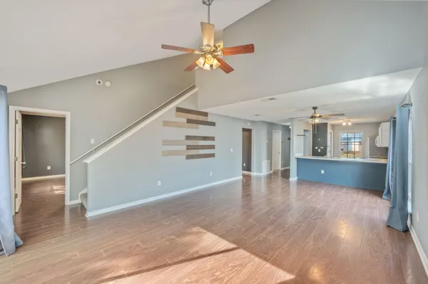 a view of an empty room with wooden floor and a ceiling fan