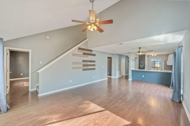 a view of an empty room with wooden floor and a ceiling fan