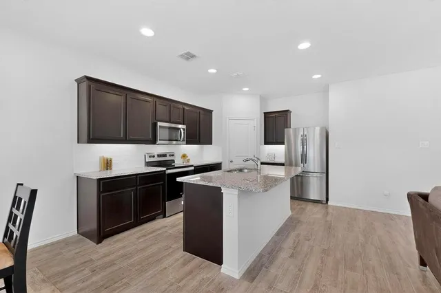 a kitchen with stainless steel appliances granite countertop a stove top oven a sink dishwasher and a refrigerator with wooden floor