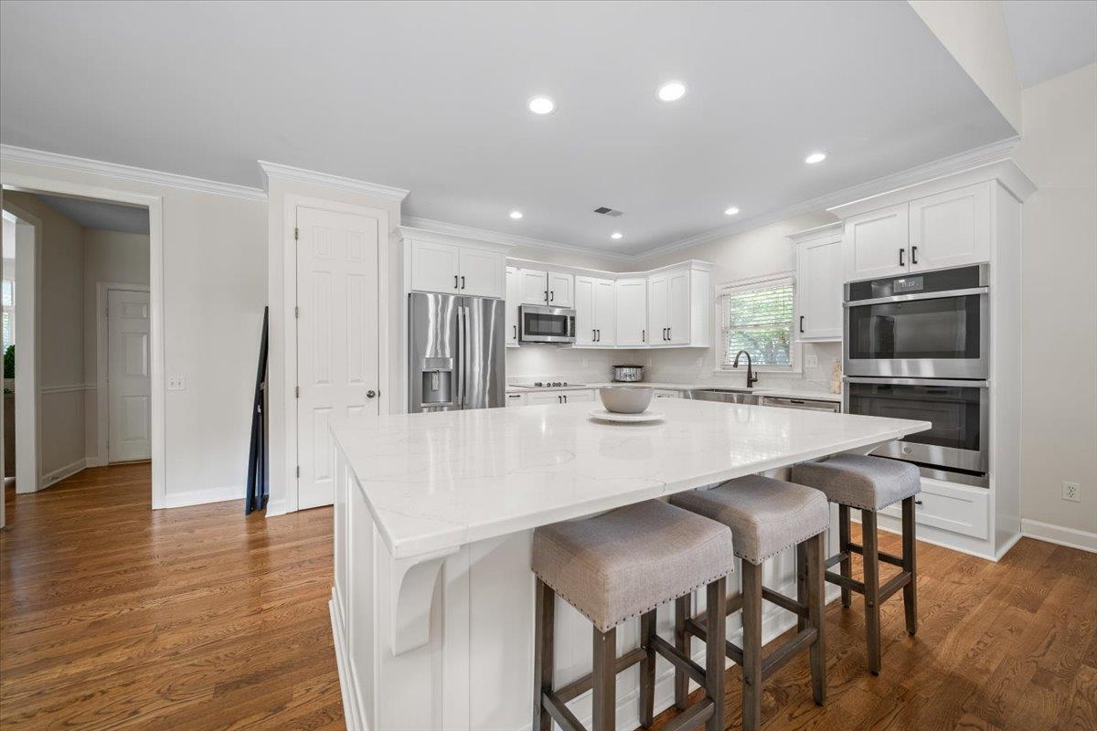 1876 Liles Lane Collierville, TN 38017 - Photo 3 of 36 Kitchen featuring a white countertop island with seating, stainless steel appliances, white cabinetry with dark hardware, and wood-finish flooring