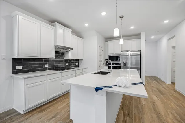 a kitchen with stainless steel appliances kitchen island granite countertop a stove a sink a refrigerator and white cabinets with wooden floor