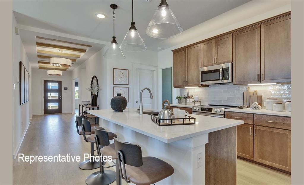 1116 Starlight Lane Nevada, TX 75442 - Photo 2 of 15 Contemporary kitchen featuring an island with seating, a stainless steel appliance suite, wood-finish cabinetry, a subway tile backsplash, and quartz countertops