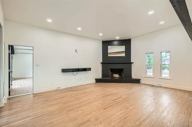 an empty room with wooden floor fireplace and windows