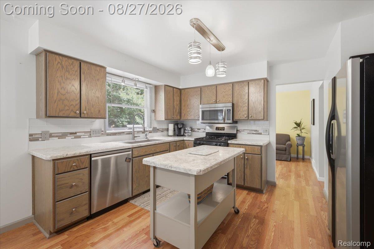 10100 Springtime Circle Clarkston, MI 48348 - Photo 20 of 73 Wood-finish flooring, wood cabinetry, stainless steel appliances, light-toned countertops, and a white tile backsplash