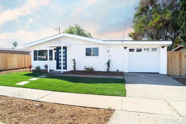 a view of a white house with a yard plants and large tree