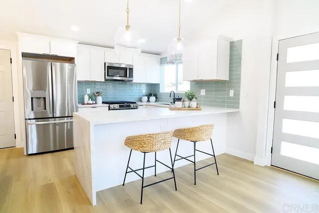 a kitchen with stainless steel appliances kitchen island granite countertop a refrigerator a stove a microwave oven a sink with island and chairs with wooden floor