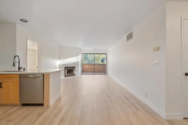 a view of a kitchen and an empty room with wooden floor and a window