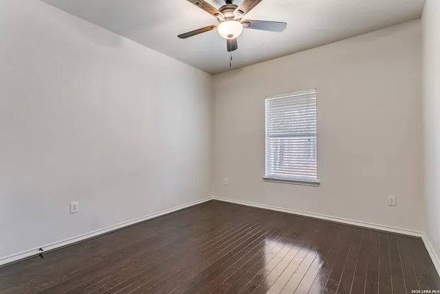 an empty room with wooden floor chandelier fan and windows