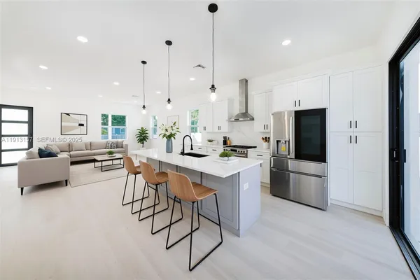 a kitchen with stainless steel appliances kitchen island granite countertop a dining table chairs and a refrigerator