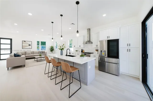 a kitchen with stainless steel appliances kitchen island granite countertop a dining table chairs and a refrigerator