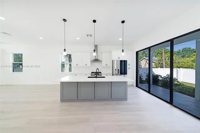a view of a kitchen with kitchen island a large window cabinets a sink and stainless steel appliances