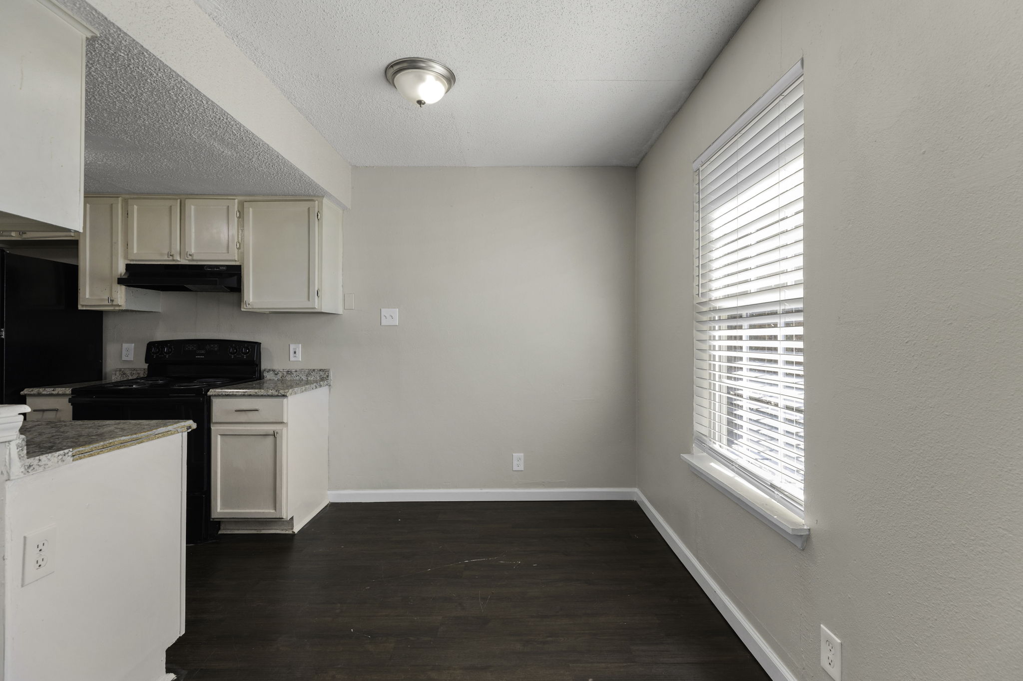 6110 Wheless Cove, Unit F Austin, TX 78723 - Photo 6 of 12 Kitchen featuring black appliances, a textured ceiling, dark wood-style floors, and light stone counters