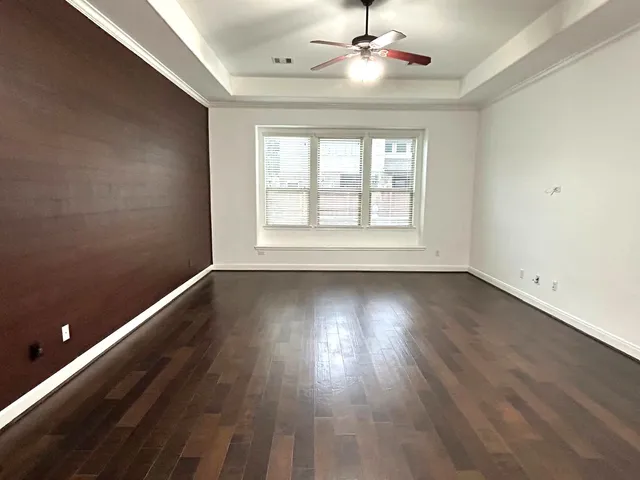 an empty room with wooden floor chandelier fan and windows