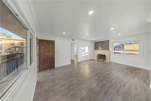 an empty room with wooden floor kitchen view and windows