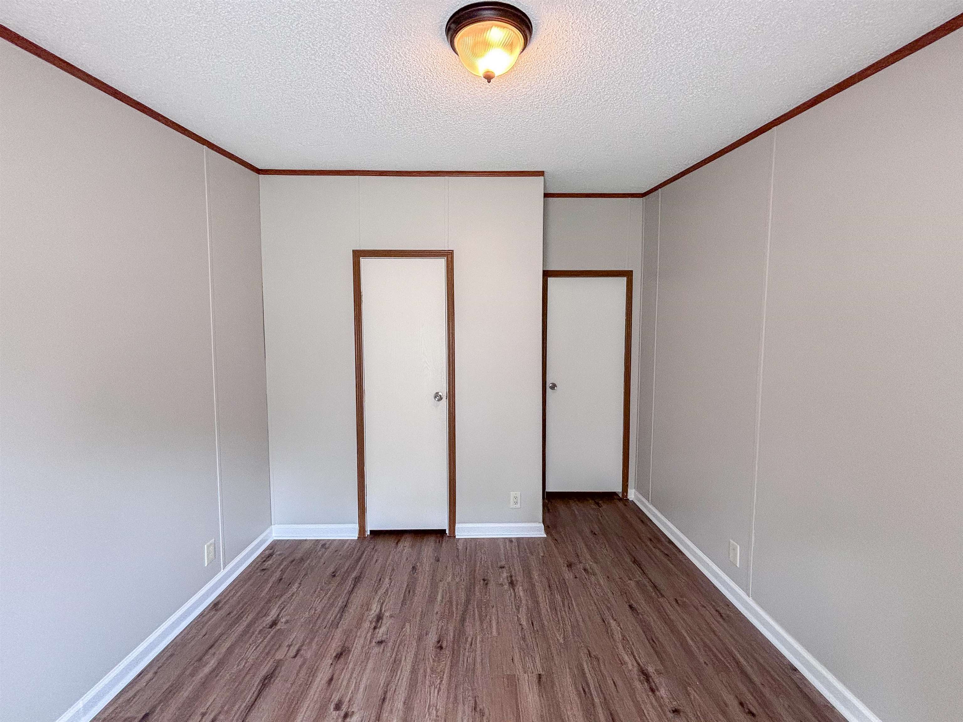 2847 Holly Grove Road Covington, TN 38019 - Photo 30 of 36 Room featuring wood-finish flooring, two white doors with brown trim, light grey wall paneling, and a ceiling-mounted light fixture