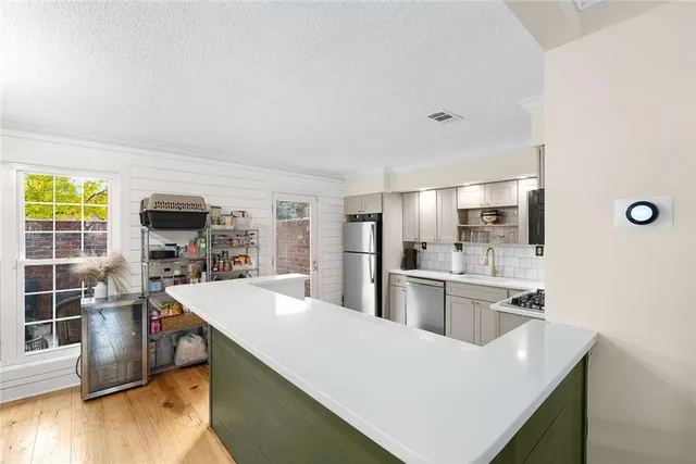 a kitchen with stainless steel appliances a stove top oven a sink dishwasher a refrigerator and white cabinets with wooden floor