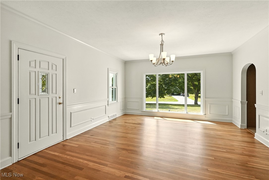 Unfurnished dining area with arched walkways, light wood-style flooring, a chandelier, and crown molding