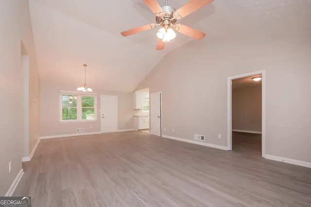 an empty room with wooden floor chandelier fan and windows
