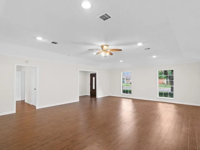 a view of an empty room with wooden floor and a ceiling fan