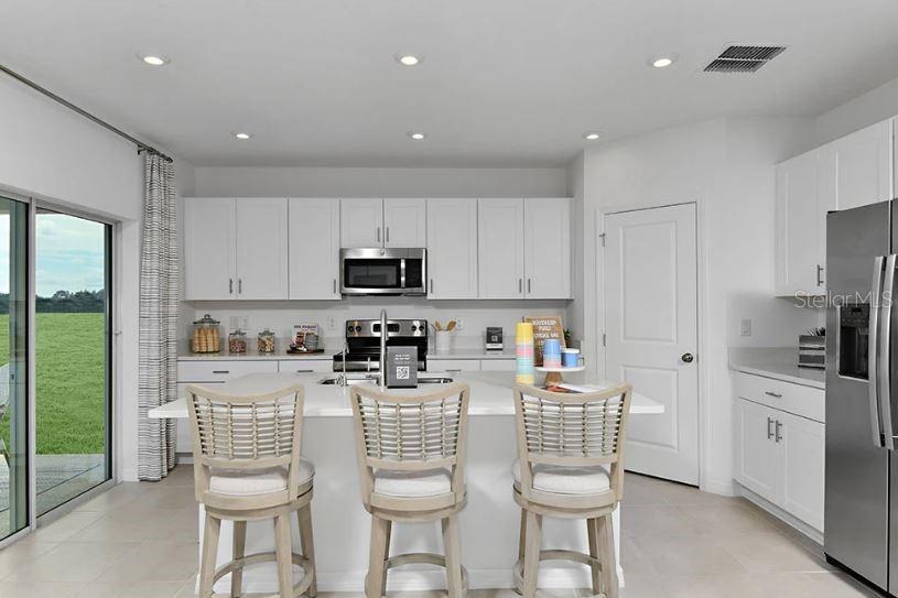 13815 Sawmill Street Parrish, FL 34219 - Photo 4 of 25 a kitchen with stainless steel appliances kitchen island granite countertop a sink a stove a refrigerator cabinets and chairs