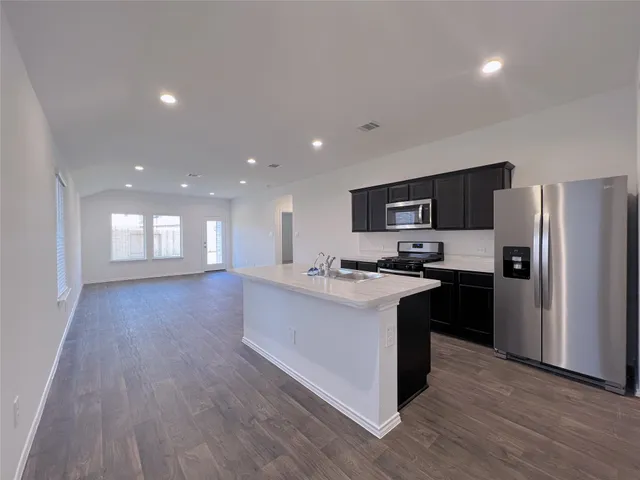 a kitchen with stainless steel appliances kitchen island granite countertop a stove top oven a sink dishwasher a refrigerator and a microwave oven with wooden floor