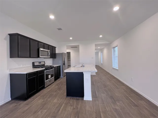 a kitchen with stainless steel appliances kitchen island granite countertop wooden floors and black cabinets