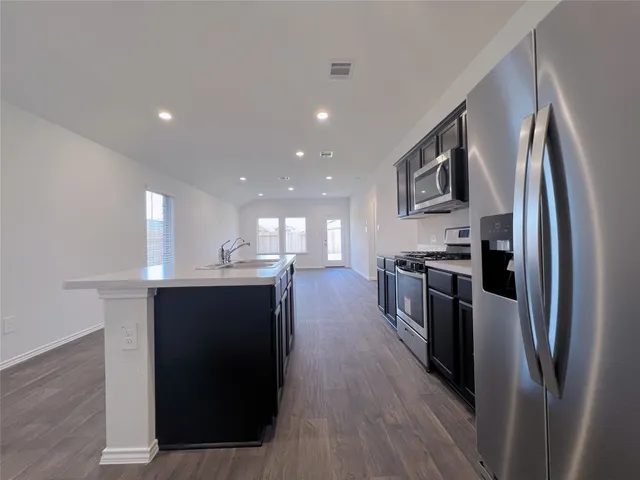 a kitchen with stainless steel appliances kitchen island granite countertop a refrigerator a sink dishwasher a stove and white cabinets with wooden floor