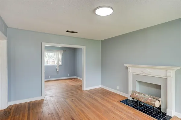 a view of an empty room with wooden floor fireplace and a window