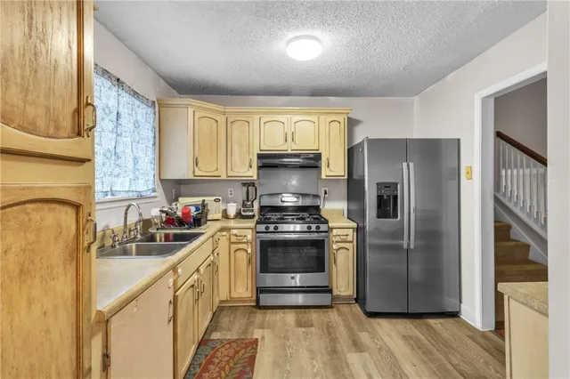 a kitchen with stainless steel appliances granite countertop a refrigerator a sink dishwasher a stove and a dining table with wooden floor