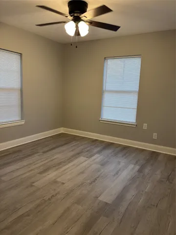 an empty room with wooden floor chandelier fan and windows