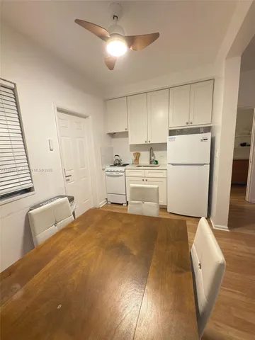 a room with stainless steel appliances kitchen island granite countertop a refrigerator a stove a sink dishwasher and white cabinets with wooden floor
