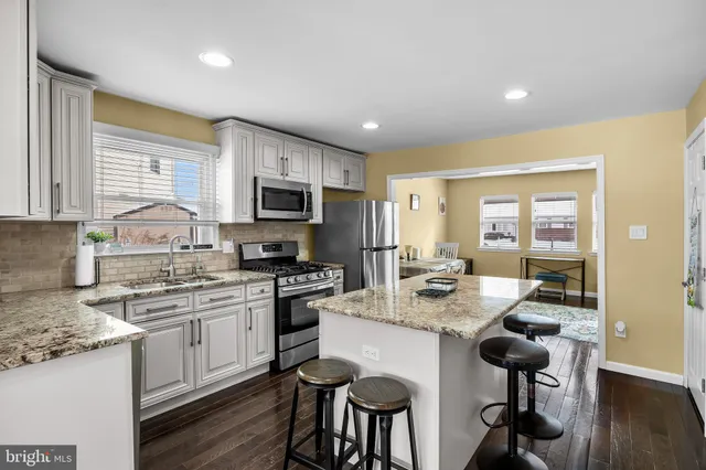 a kitchen with stainless steel appliances granite countertop a stove top oven a sink dishwasher a dining table and chairs with wooden floor