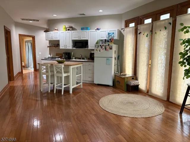 a kitchen with stainless steel appliances kitchen island granite countertop a refrigerator a stove and white cabinets with wooden floor