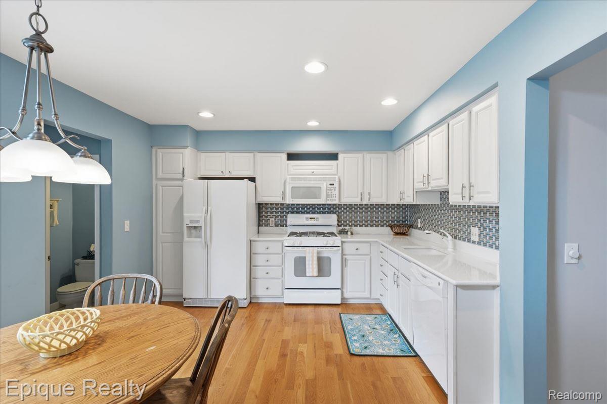 26 Kirks Court Rochester, MI 48309 - Photo 15 of 44 Kitchen featuring light wood-finish flooring, white cabinetry with silver hardware, white appliances, and a blue and white patterned tile backsplash