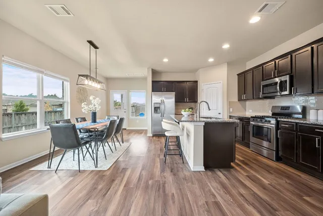 a kitchen with stainless steel appliances granite countertop a stove top oven a sink dishwasher a dining table and chairs with wooden floor