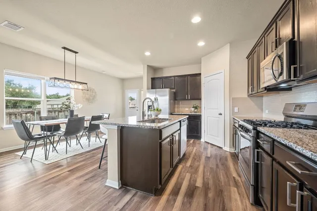 a kitchen with stainless steel appliances granite countertop a table chairs stove and wooden floor