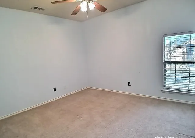 an empty room with a chandelier fan and windows