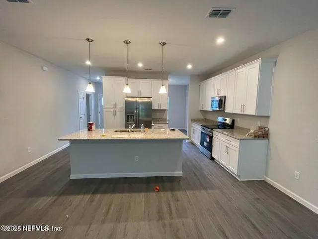 a large white kitchen with kitchen island a sink dishwasher a stove and a refrigerator with wooden floor