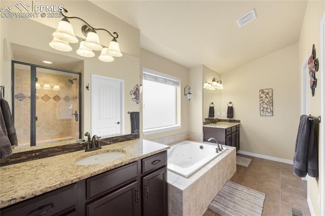1131 Old North Gate Road Colorado Springs, CO 80921 - Photo 17 of 39 Full bathroom with a stall shower, a jetted tub, two vanities, vaulted ceiling, and tile patterned flooring