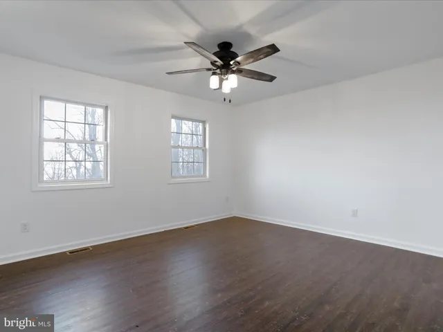 an empty room with wooden floor fan and windows