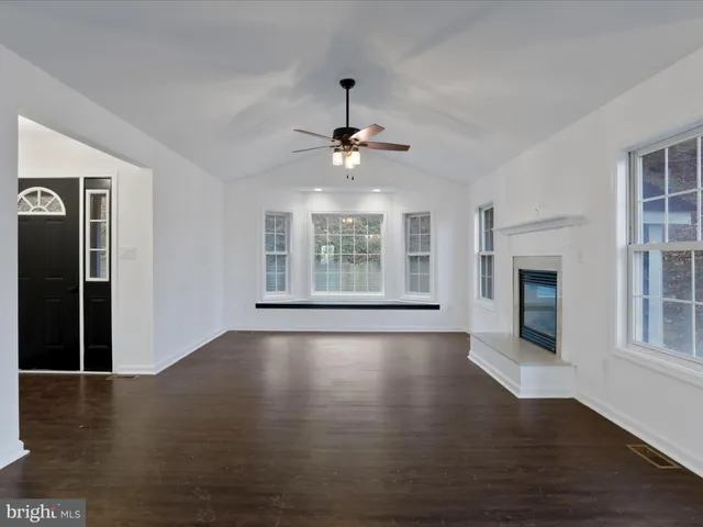 a view of an empty room with wooden floor fireplace and a window