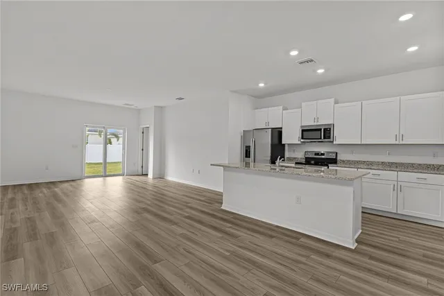 a kitchen with stainless steel appliances granite countertop a stove a sink a refrigerator white cabinets and wooden floor