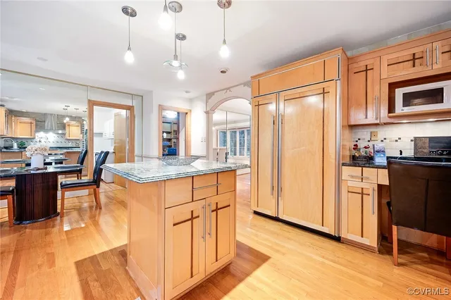 a kitchen with stainless steel appliances granite countertop a refrigerator a oven a dining table and chairs with wooden floor