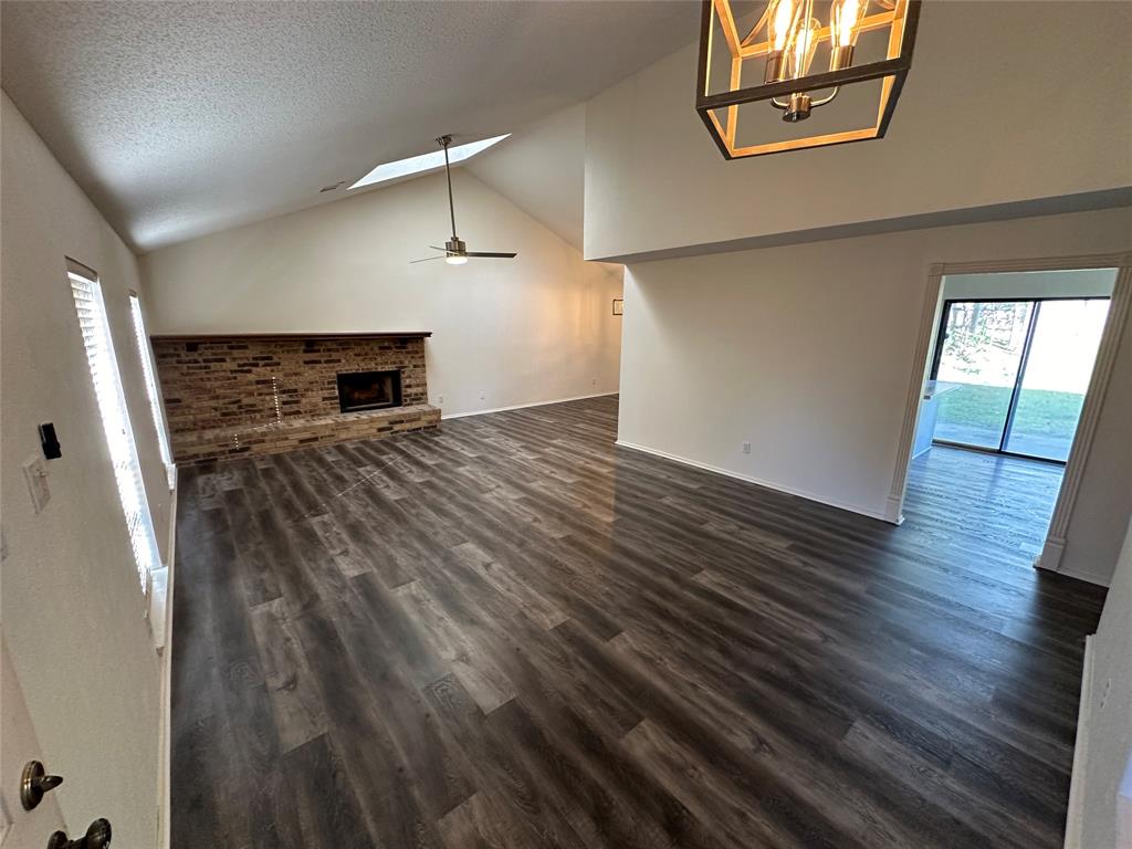 307 Harrington Lane Euless, TX 76039 - Photo 4 of 20 Unfurnished living room with a brick fireplace, ceiling fan, dark wood finished floors, a skylight, and high vaulted ceiling