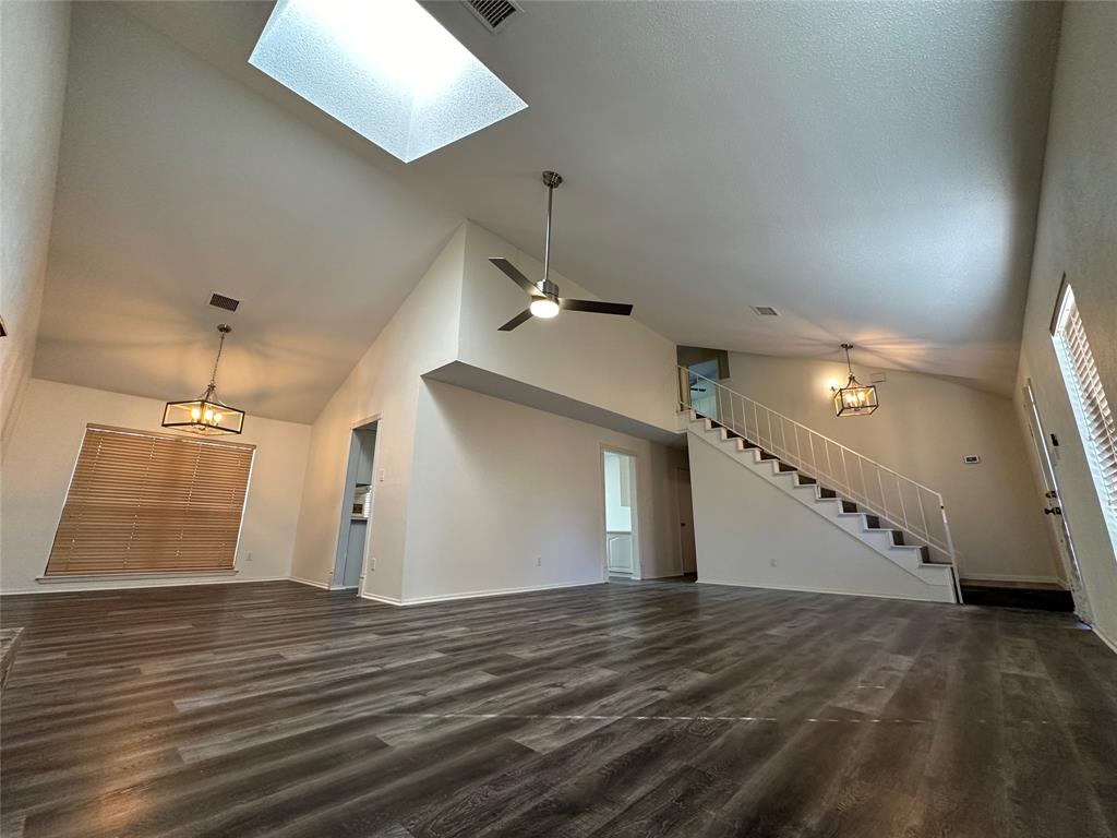 307 Harrington Lane Euless, TX 76039 - Photo 5 of 20 Unfurnished living room featuring a chandelier, dark wood-style floors, stairs, high vaulted ceiling, and a skylight