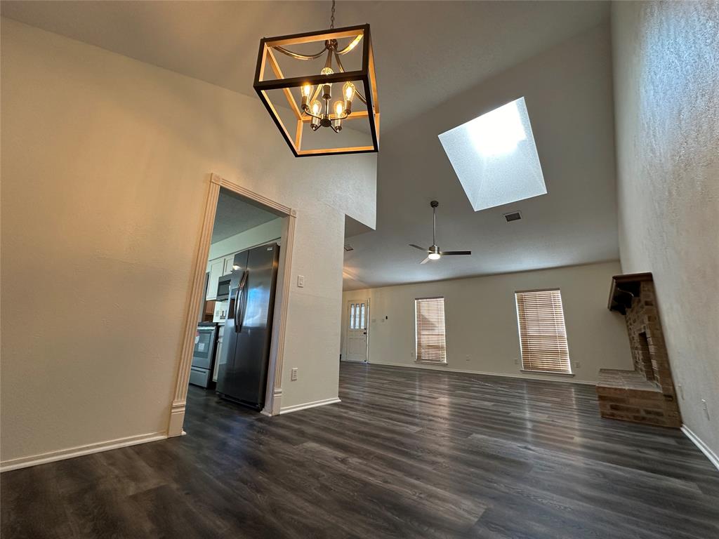 307 Harrington Lane Euless, TX 76039 - Photo 6 of 20 Unfurnished living room with ceiling fan, dark wood finished floors, high vaulted ceiling, a chandelier, and a skylight