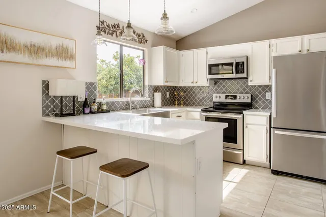 a kitchen with stainless steel appliances granite countertop a sink a stove a refrigerator cabinets and chairs